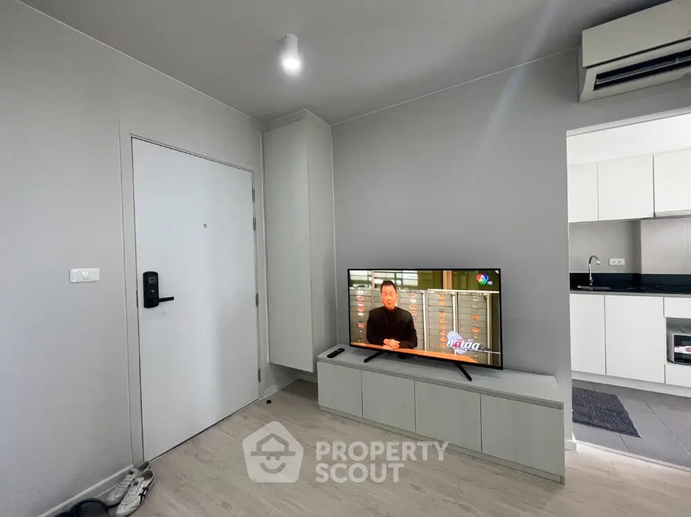 Modern living room with sleek TV setup and adjacent kitchen area in stylish apartment.