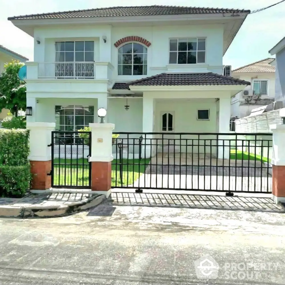 Charming two-story house with gated entrance and lush green lawn in a serene neighborhood.