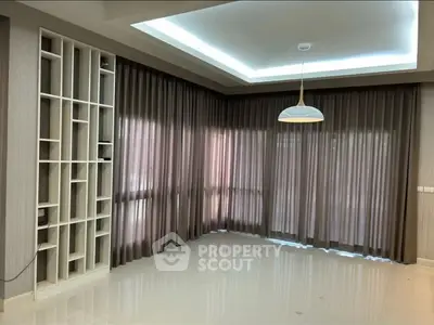 Spacious empty living room with modern ceiling light and large windows with curtains.