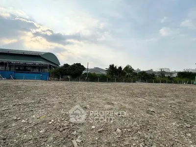 Expansive vacant land with potential for development, surrounded by greenery and partial building view.