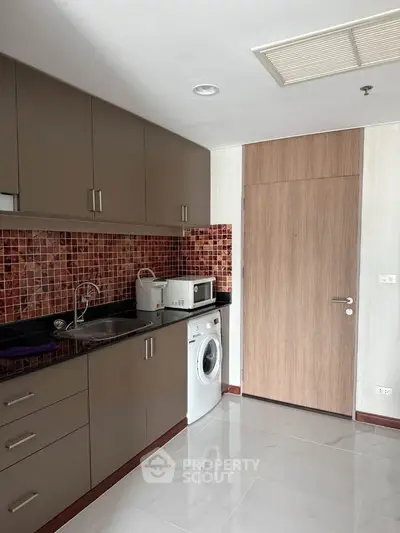 Modern kitchen with sleek cabinets, washing machine, and mosaic backsplash