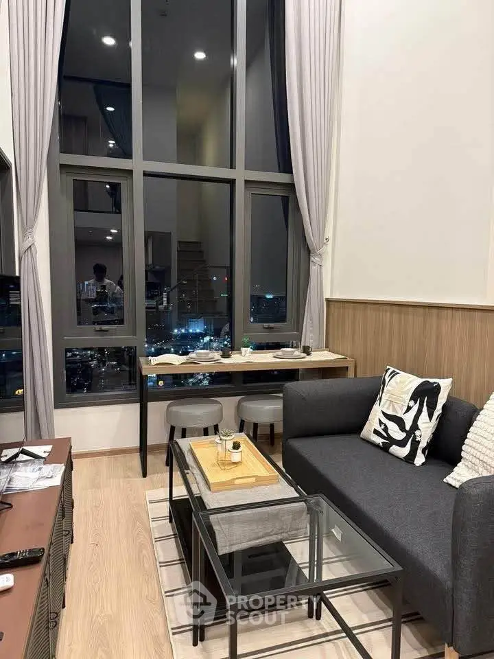 Modern living room with high ceilings and city view through large windows.