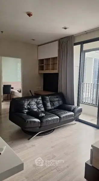 Modern living room with sleek black sofa and large window balcony access.