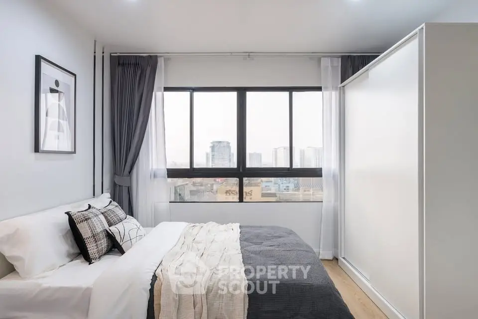 Modern bedroom with large window offering city view, stylish decor, and cozy bedding.