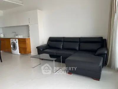 Modern living room with sleek black leather sofa and integrated kitchen featuring a washing machine.