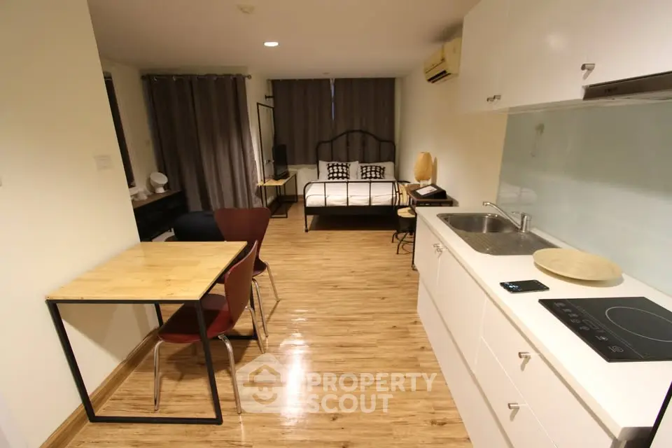Modern studio apartment with open kitchen and cozy living area, featuring wooden flooring and stylish decor.