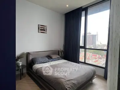 Modern bedroom with large window offering city view, featuring cozy bed and stylish decor.