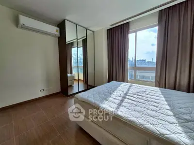 Bright bedroom with large window and mirrored wardrobe, featuring a comfortable bed and air conditioning.