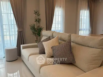 Elegant living room with plush beige sofa and stylish cushions, bathed in natural light from large windows.