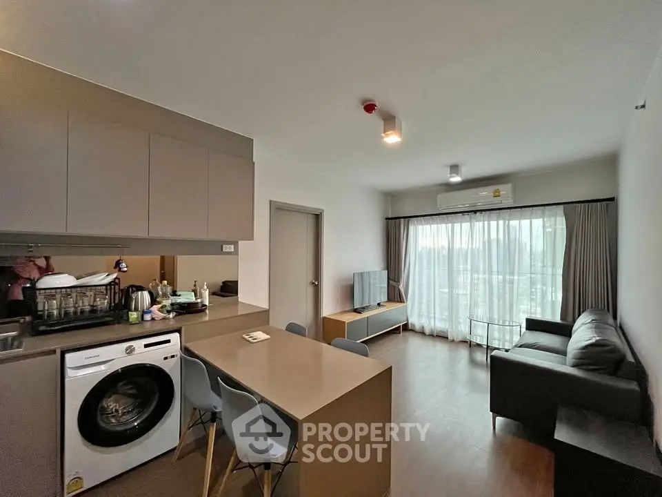 Modern open-plan living room with kitchen, featuring sleek furniture and natural light.