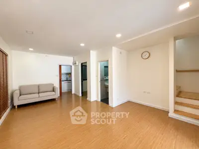 Spacious living room with modern design and wooden flooring, featuring a cozy sofa and wall clock.