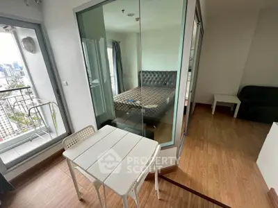 Modern apartment with glass-walled bedroom and city view balcony, featuring stylish furniture and wooden flooring.