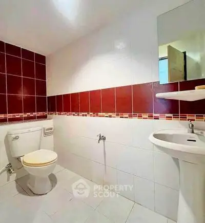 Modern bathroom with red and white tiles, featuring a toilet and sink.