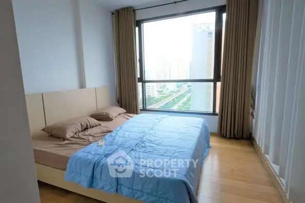 Spacious bedroom with large window offering stunning city view, perfect for urban living.