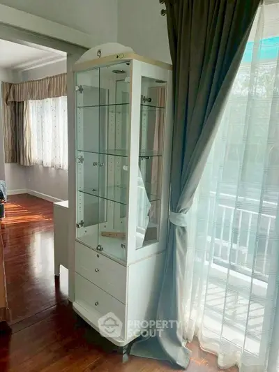 Elegant corner unit with glass display cabinet and large windows in a bright living room.