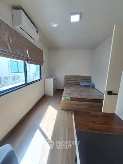 Cozy bedroom with wooden flooring, large window, and air conditioning unit.