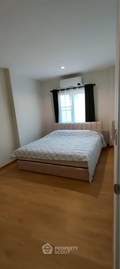 Cozy bedroom with wooden flooring and large window, featuring a comfortable bed and air conditioning.