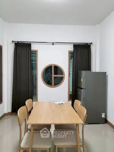 Modern dining area with wooden table and chairs, featuring a unique circular window and sleek refrigerator.