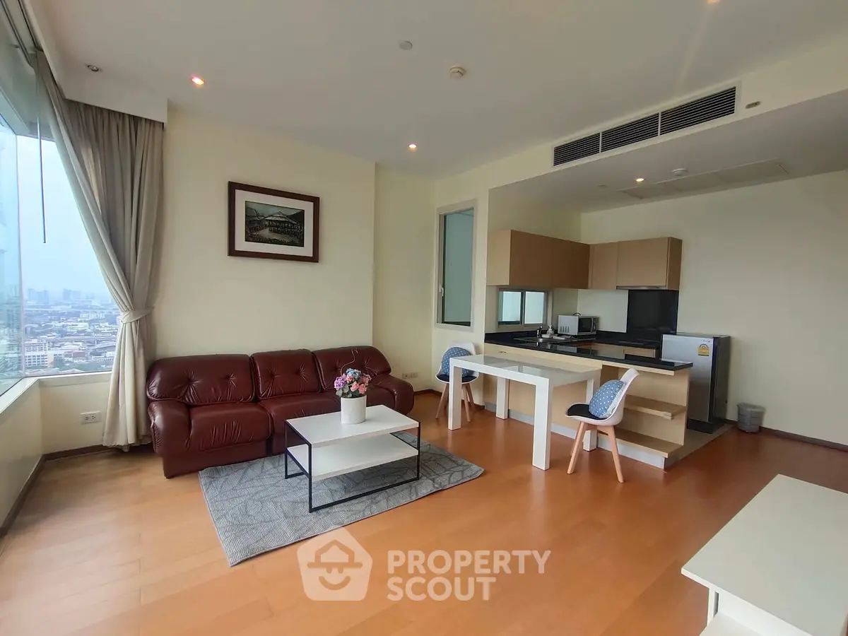 Spacious living room with open kitchen and city view, featuring modern furniture and wooden flooring.