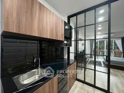 Modern kitchen with sleek black countertops and wooden cabinets, open layout to living area with balcony view.