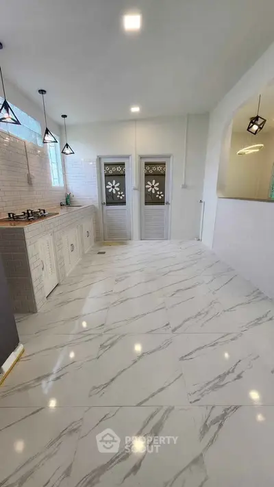 Spacious kitchen with marble flooring and modern lighting in a stylish home.