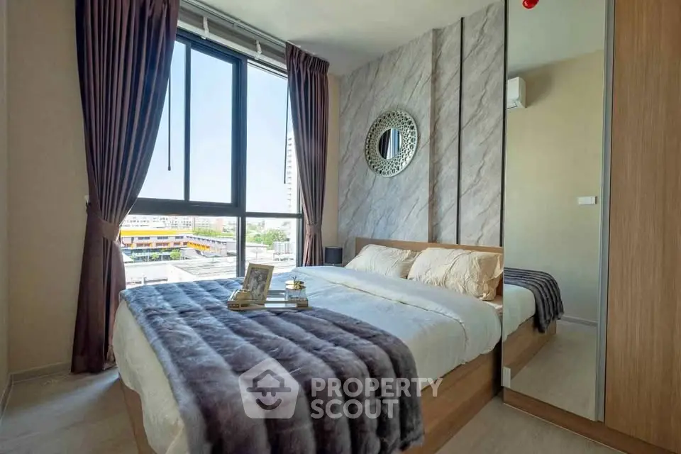 Modern bedroom with large window and stylish decor in urban apartment.