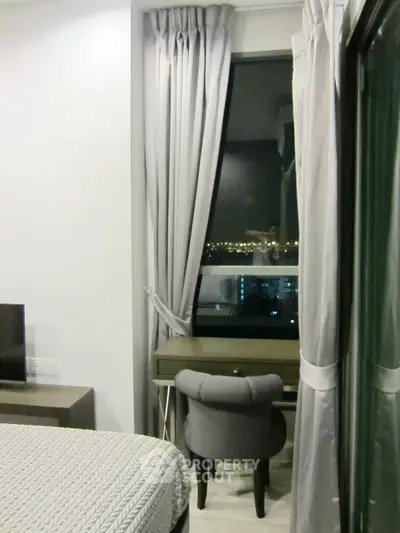 Cozy bedroom with city view, elegant curtains, and stylish desk chair.