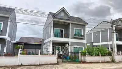 Modern two-story gray house with balcony and fenced yard in suburban neighborhood.
