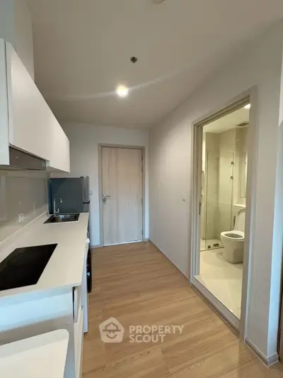Modern compact kitchen with sleek white cabinetry and adjacent bathroom in a contemporary apartment.