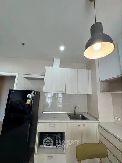 Modern kitchen with sleek cabinetry, black fridge, and stylish lighting in a contemporary apartment.