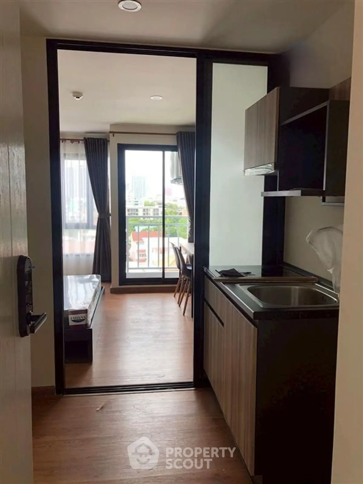 Modern apartment interior with compact kitchen and bright living area featuring large windows.