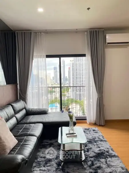 Modern living room with city view, sleek black sofa, and stylish decor.