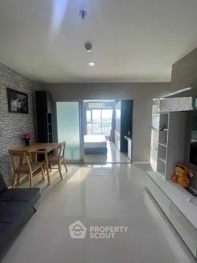 Modern living room with sleek furniture and bright natural light, leading to a cozy bedroom with a view.