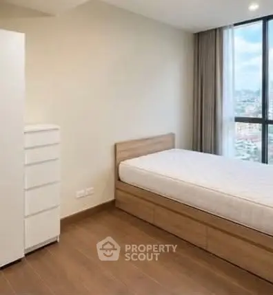 Modern minimalist bedroom with wooden flooring and large window offering city views.