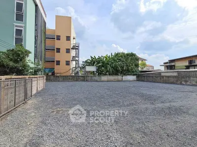 Spacious vacant lot with gravel surface, ideal for development, surrounded by buildings and greenery.