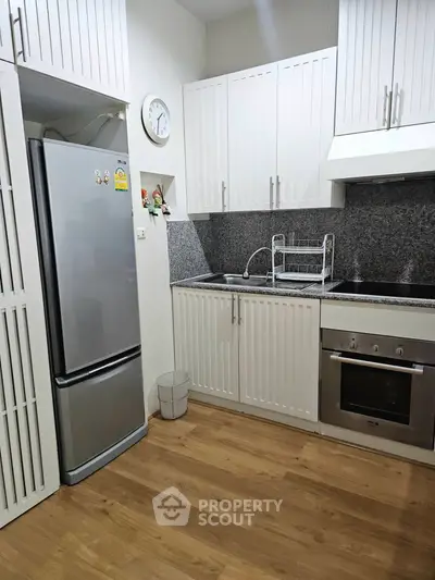 Modern kitchen with sleek white cabinets, stainless steel fridge, and built-in oven in a cozy apartment.