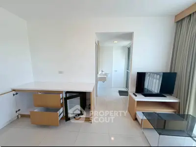 Modern living room with sleek furniture and open layout, featuring a TV and mini fridge.