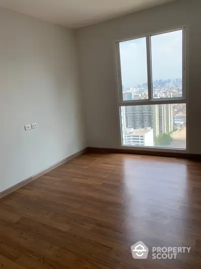 Bright empty room with wooden flooring and city view from large window.