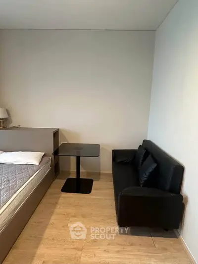 Modern minimalist bedroom with sleek black sofa and compact table, perfect for urban living.