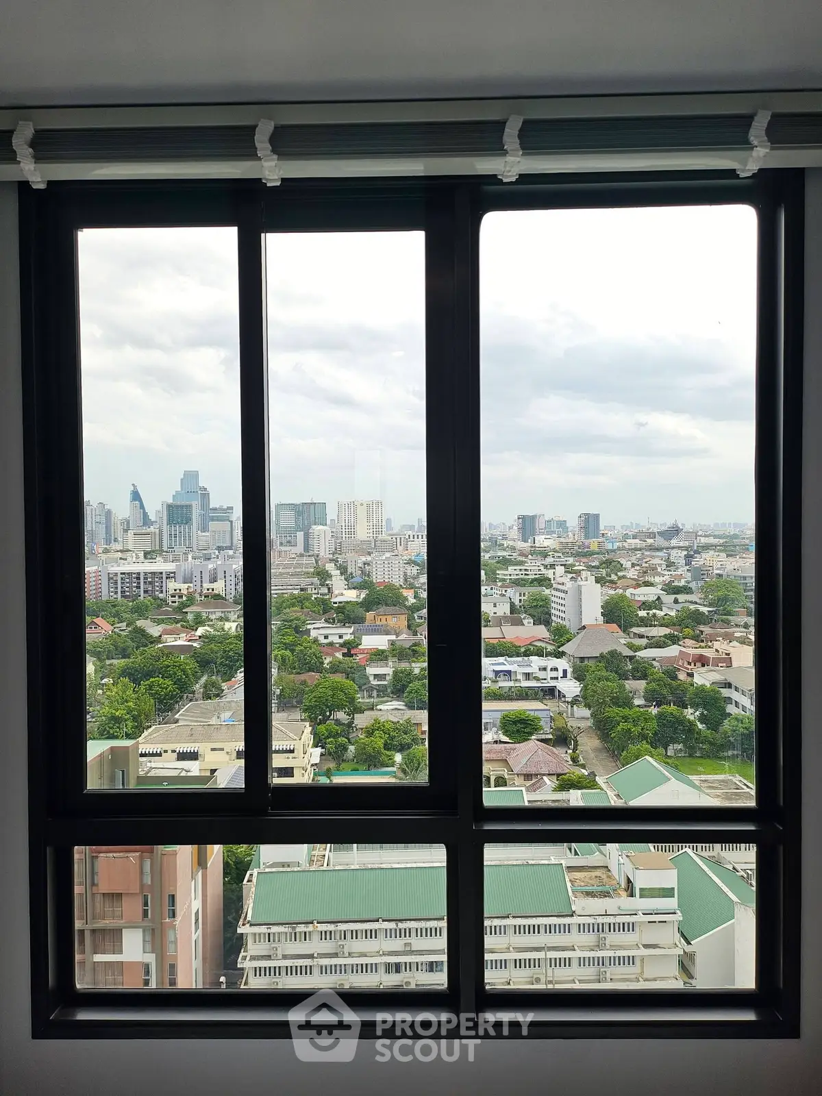 Stunning cityscape view from a high-rise apartment window, showcasing urban skyline and greenery.