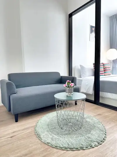 Modern living room with sleek gray sofa and stylish glass coffee table, adjacent to a cozy bedroom.