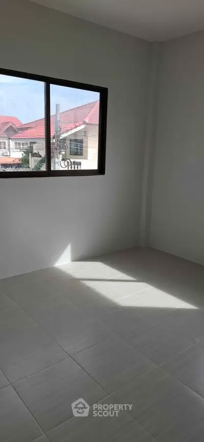 Bright empty room with large window and tiled floor, offering potential for customization.