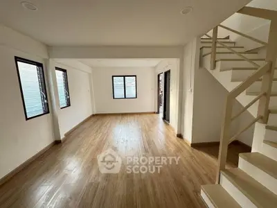 Spacious open-plan living room with wooden flooring and modern staircase, ideal for contemporary living.