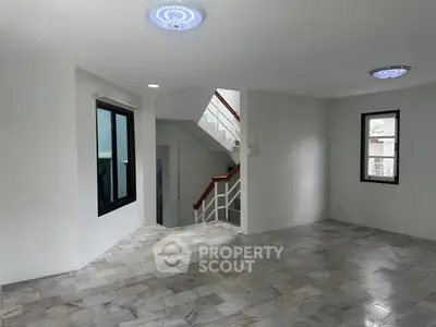 Spacious modern living room with marble flooring and staircase, ample natural light.