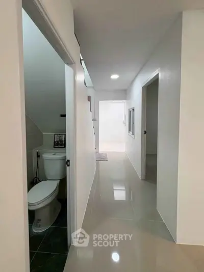 Modern hallway with glossy tiles and a small bathroom entrance, showcasing minimalist design.