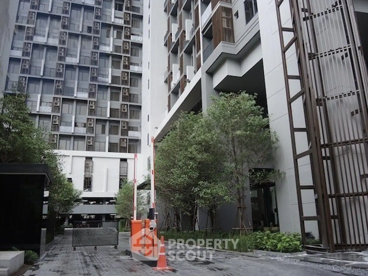 Modern high-rise building entrance with lush greenery and secure access gate.