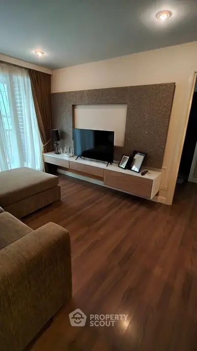 Modern living room with stylish decor and large TV, featuring hardwood floors and natural light.