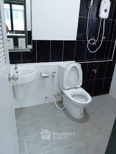 Modern bathroom with sleek black and white tiles, featuring a toilet, sink, and shower heater.