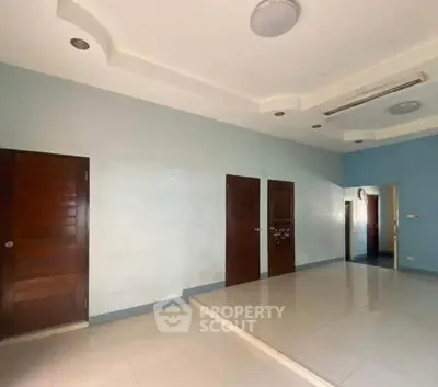 Spacious room with tiled flooring and modern ceiling lights, featuring multiple wooden doors.
