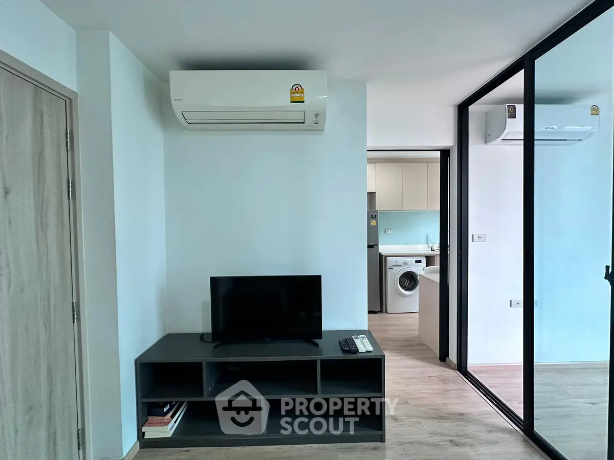 Modern living room with air conditioning and TV, open view to kitchen with washing machine.